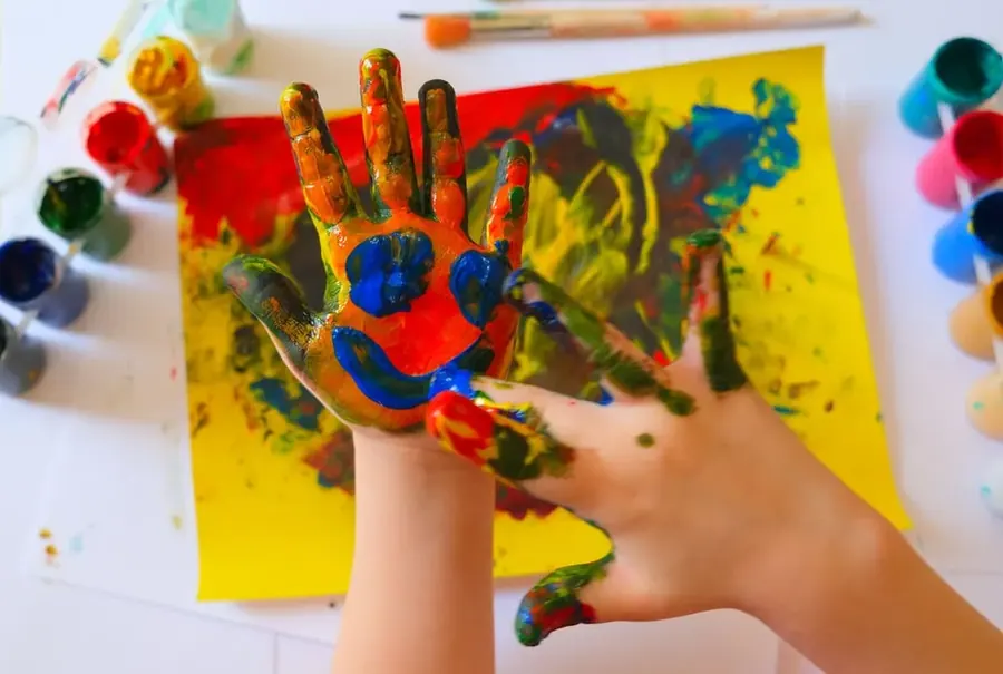 A child's paint-covered hands on a sheet of paper